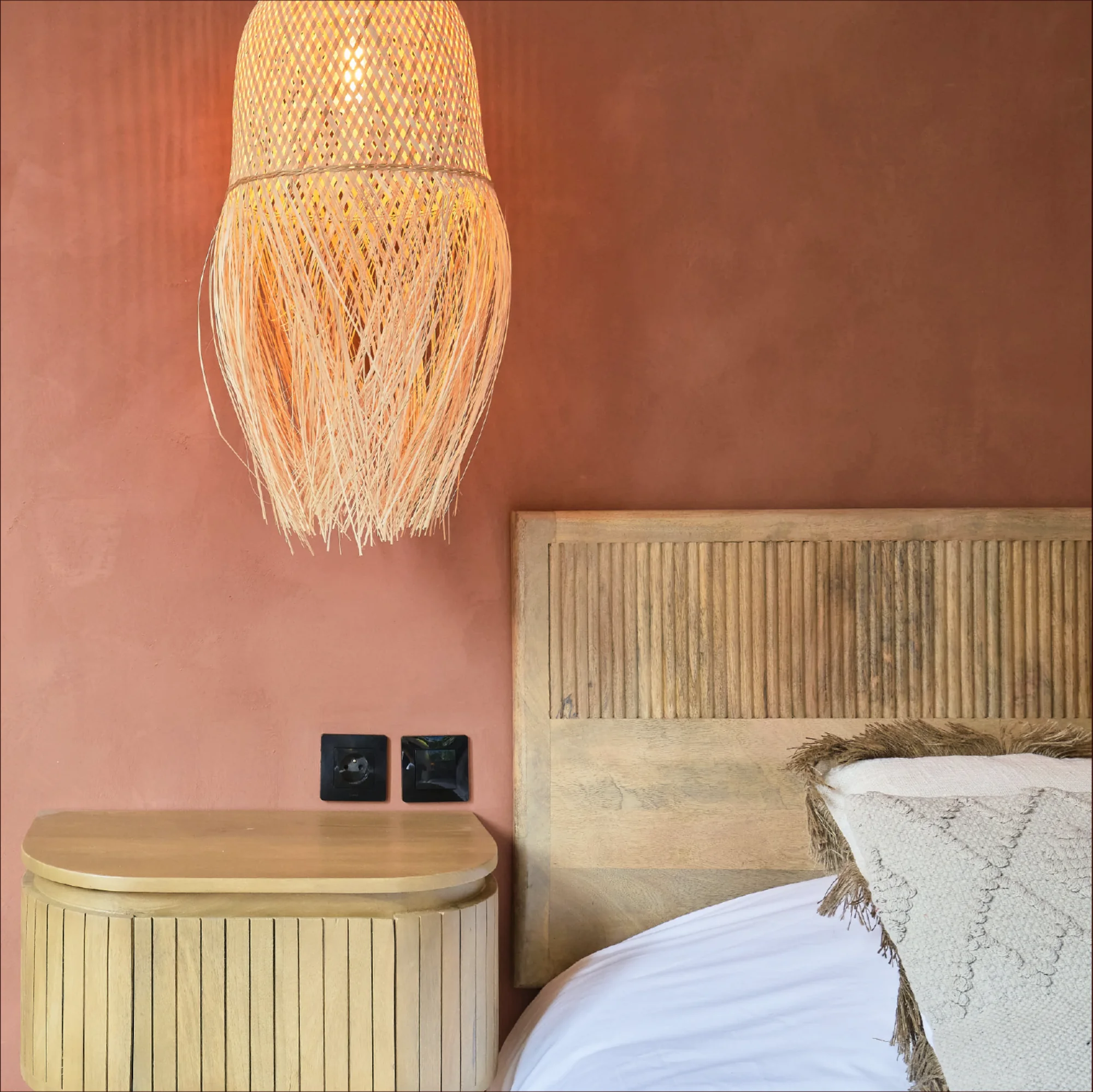 Chambre Casa Del Spa : lampe en fibres naturelles, mur terracotta, tête de lit en bois cannelé.