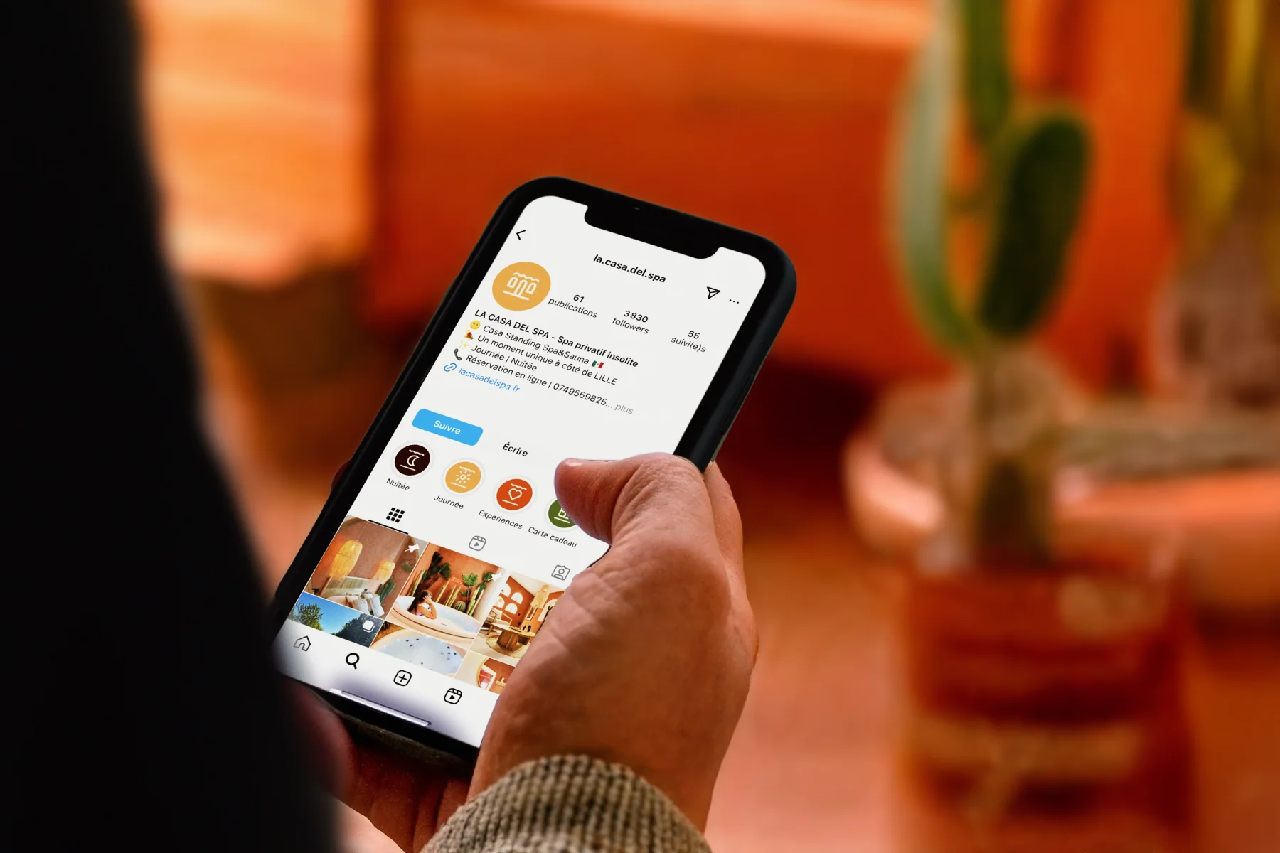 Casa Del Spa, mockup digital : profil Instagram la.casa.del.spa sur iPhone tenu en main, fond terracotta hors focus, logos et highlights forfaits visibles.