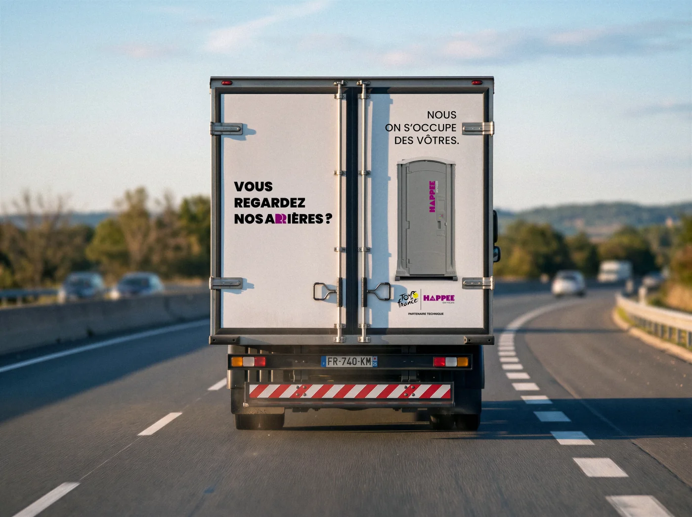 Arrière du camion Happee, message Vous regardez nos arrières, Nous on s'occupe des vôtres en blanc sur fond clair, cabine WC visible.