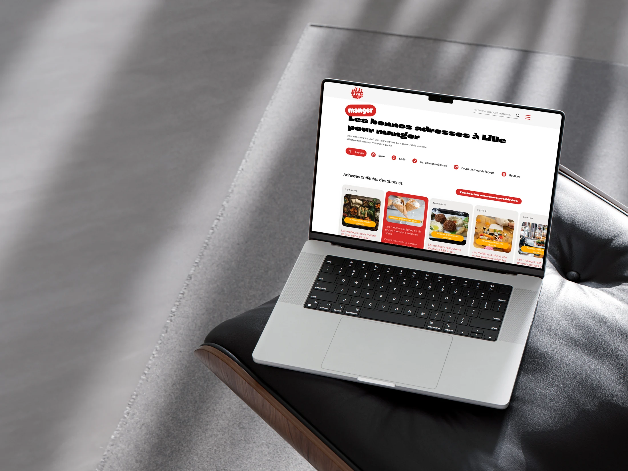 Lille Addict, mockup laptop posé sur sofa cuir, page Manger avec sélections d'adresses lilloises.